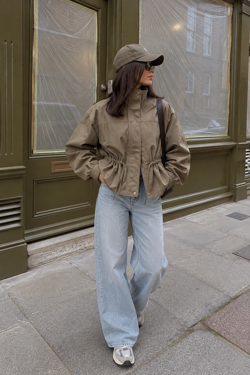 Vrouw draagt Jasje Camille in legergroen met wide leg jeans en pet