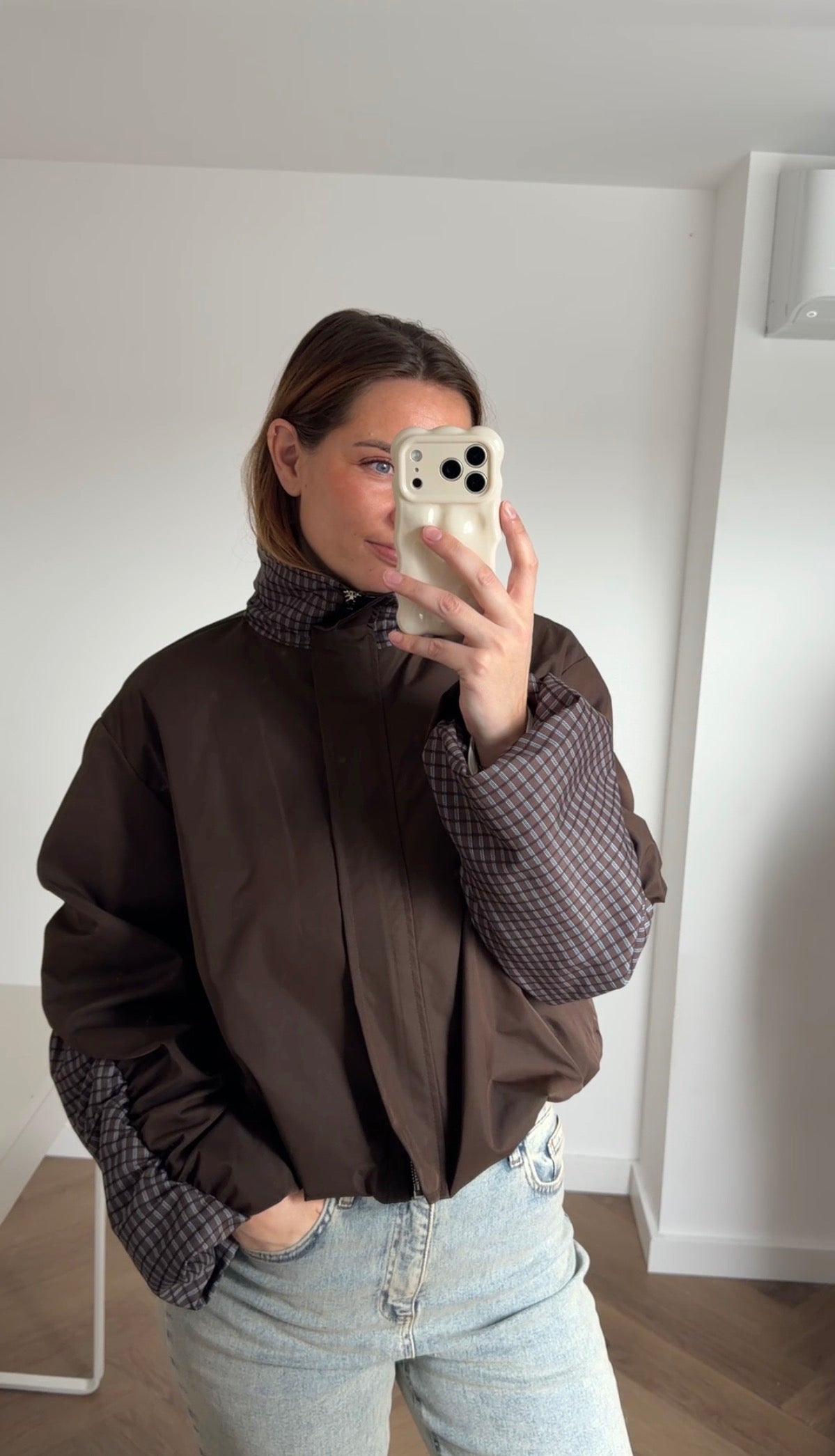 Model draagt de Jules Check Jacket, een kort donkerbruin damesjasje met geruite kraag en mouwen en een lichtblauwe jeans