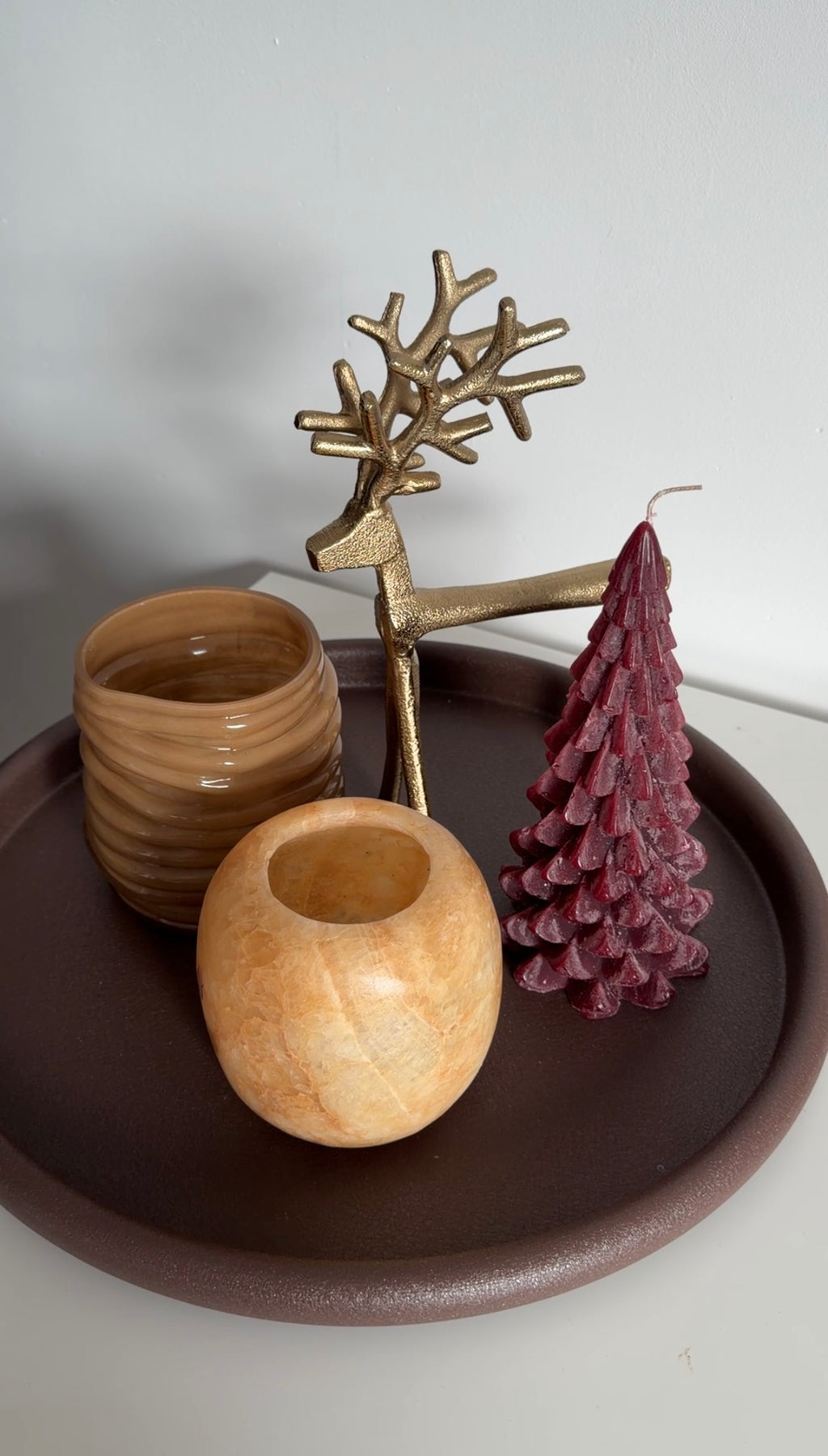 Kerstboomkaars in diepe burgundy kleur met warme bruine woonaccessoires op een dienblad