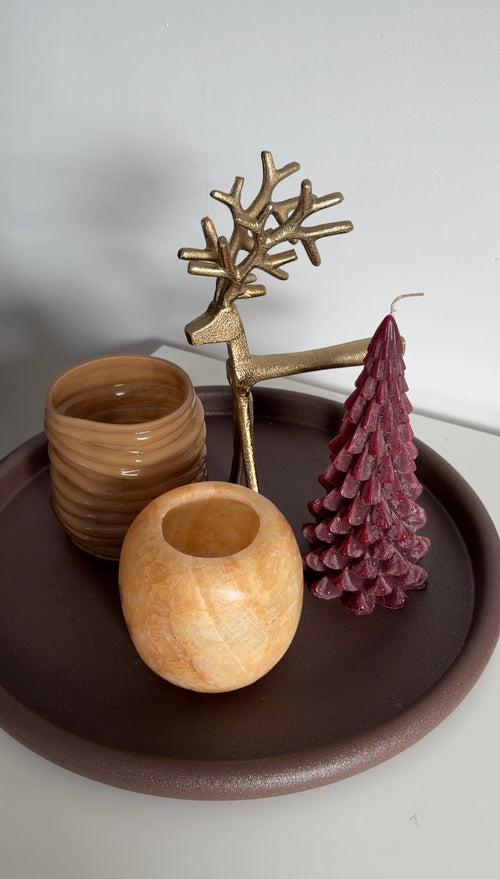 Kerstboomkaars in diepe burgundy kleur met warme bruine woonaccessoires op een dienblad